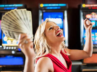 Happy mid adult woman winning money on a slot machine in a casino and celebrating.